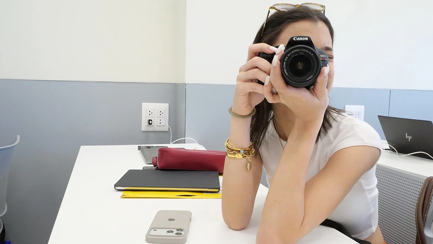 Estudiante sostiene la cámara frente a su rostro, lista para tomar una fotografía, 
